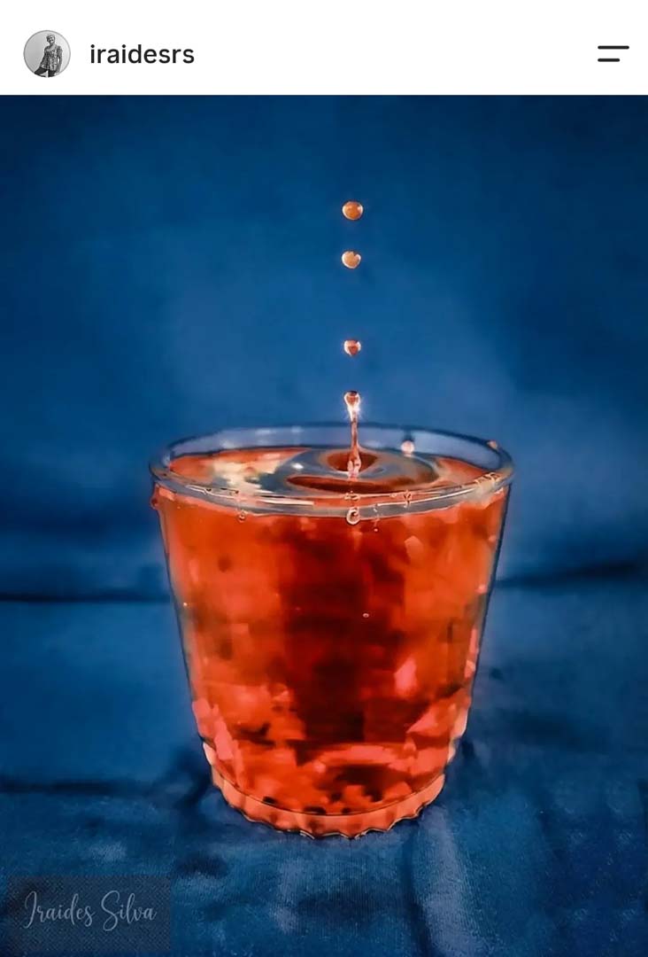 Copo com respingo de líquido vermelho e fundo azul, foto de still life feita com celular por aluno do curso