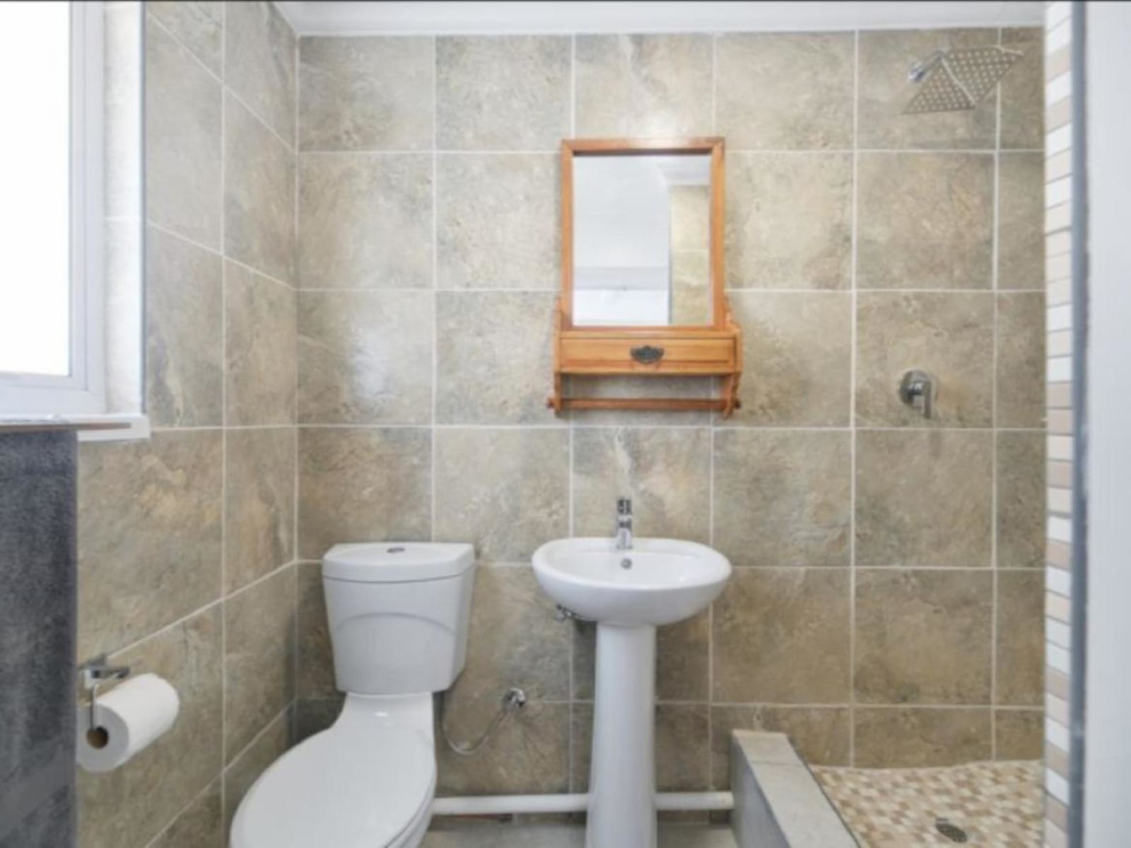 One of five en-suite bathrooms at Gans-te-Ver — stone-tiled walk-in shower with a rain head, basin and a wooden-framed mirror.