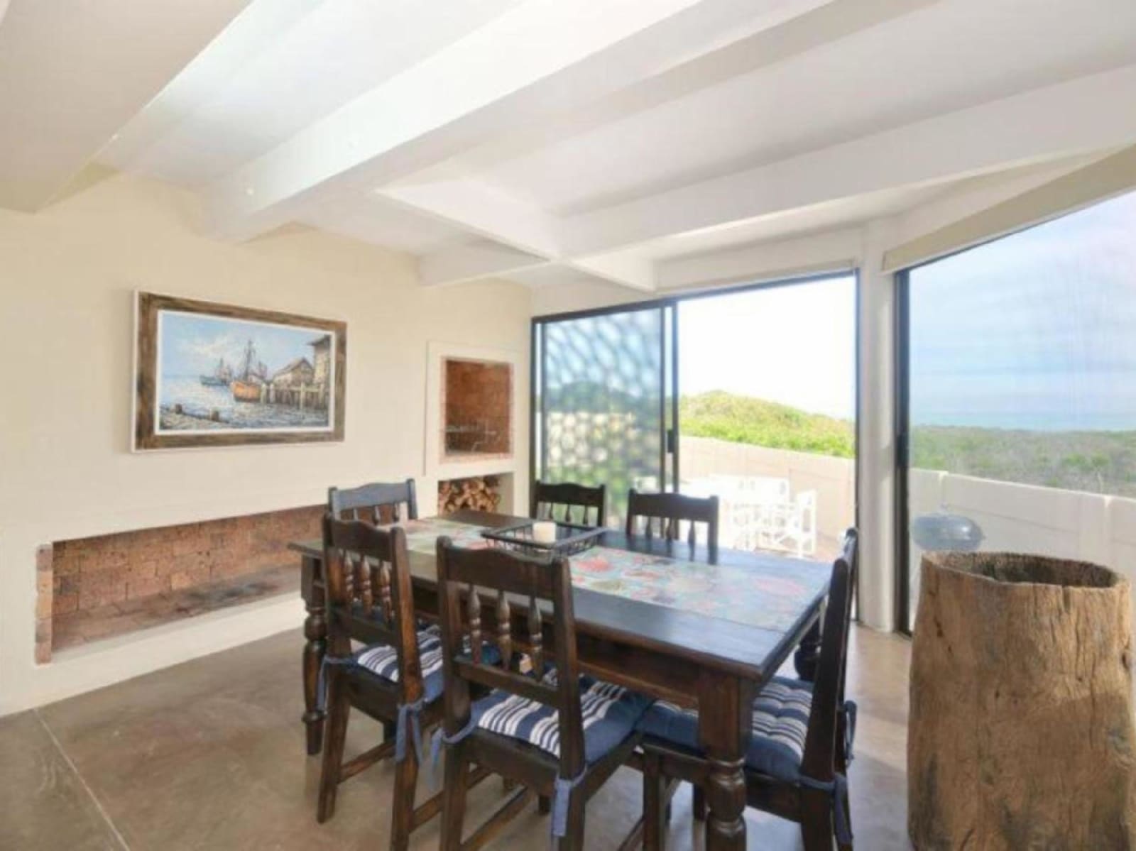 The six-seater dining table at Gans-te-Ver beside the indoor braai, with sliding doors opening to the terrace and the dunes beyond.