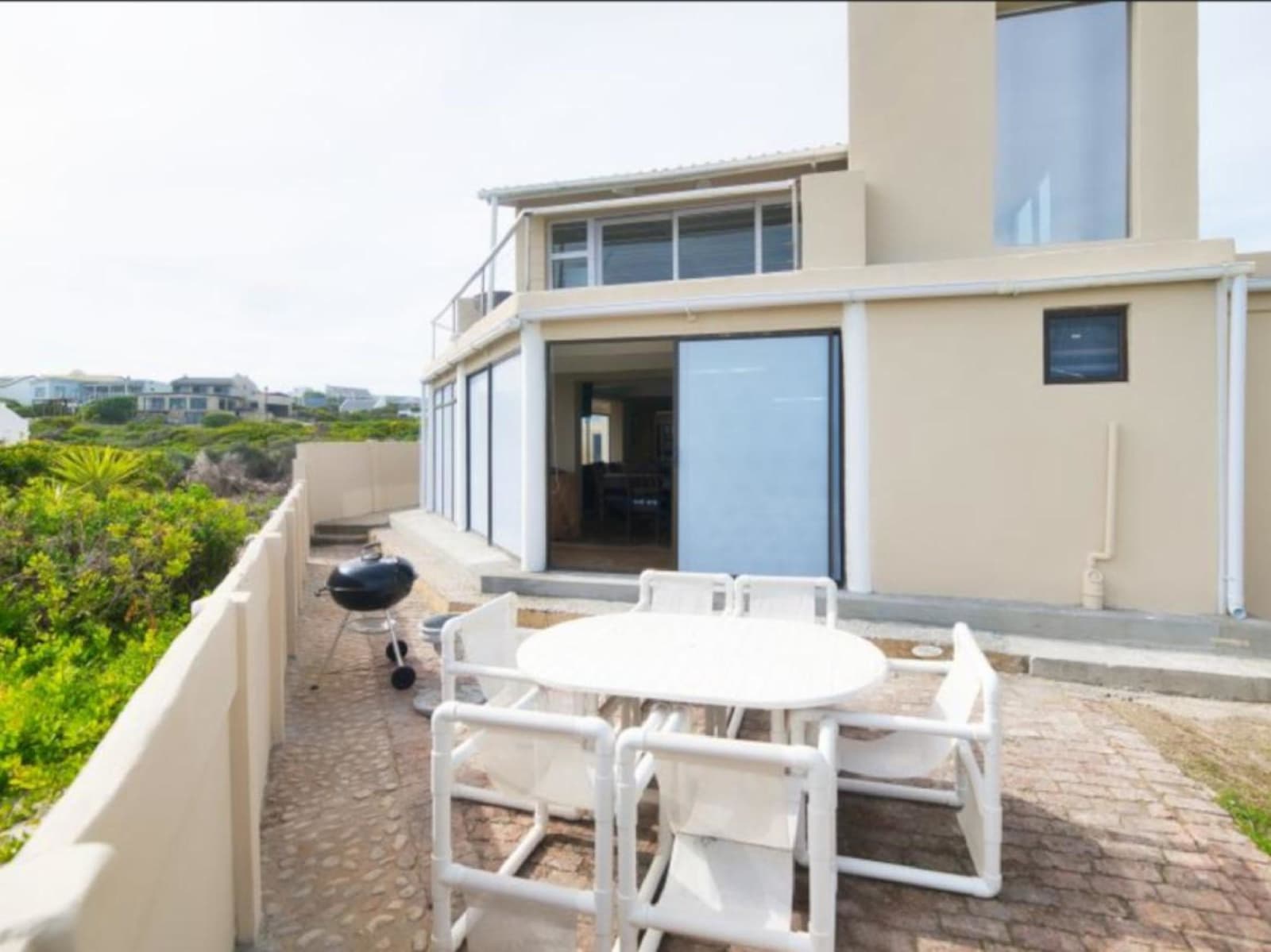Gans-te-Ver from the side terrace — a double-storey beach house with floor-to-ceiling glass, white walls and the braai patio in front.