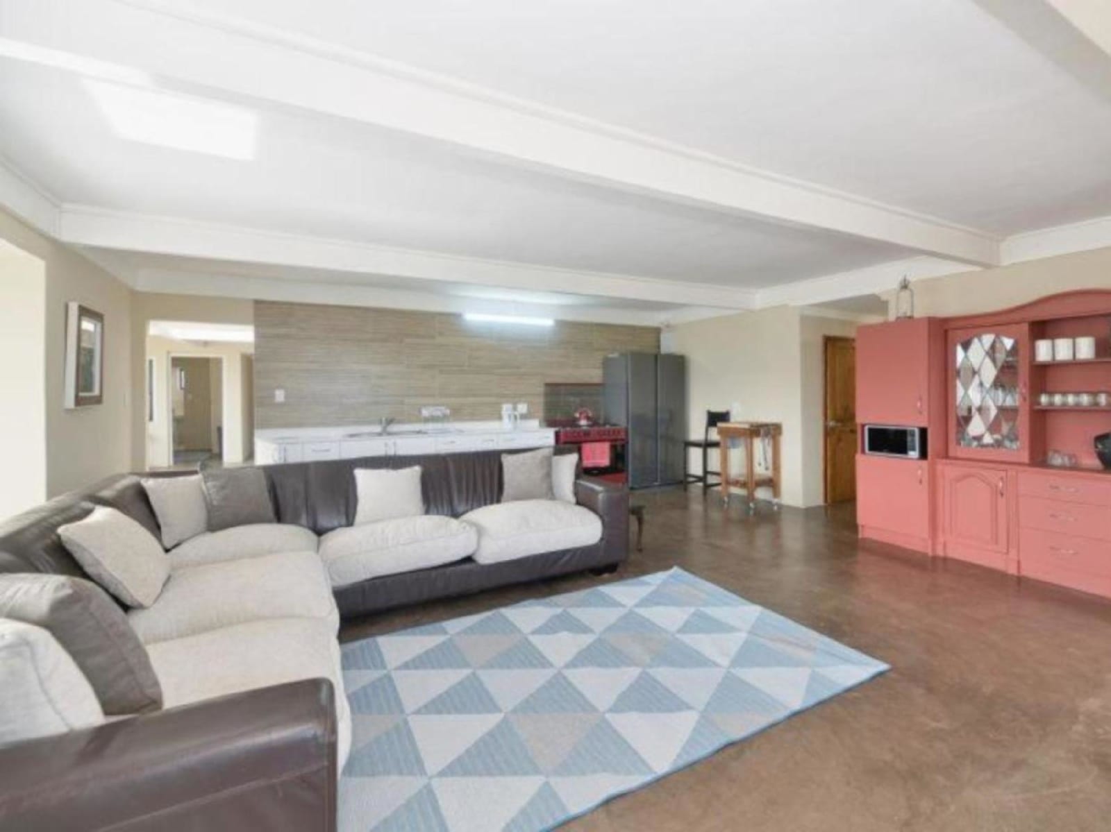 The main open-plan lounge at Gans-te-Ver — a big corner couch around a soft blue rug, with the kitchen and its red gas stove behind.