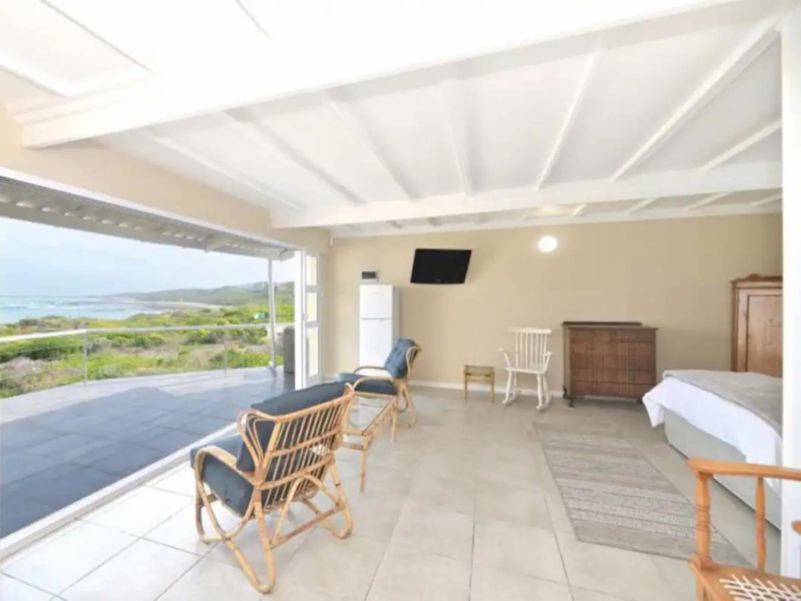 The main suite at Gans-te-Ver opening onto its private balcony — glass balustrade, the dunes and the sea beyond the bed.