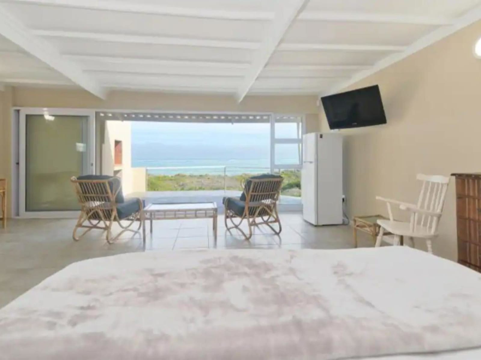The main suite at Gans-te-Ver — from the bed, the room opens straight onto the sea-view balcony with rattan chairs and its own fridge and TV.