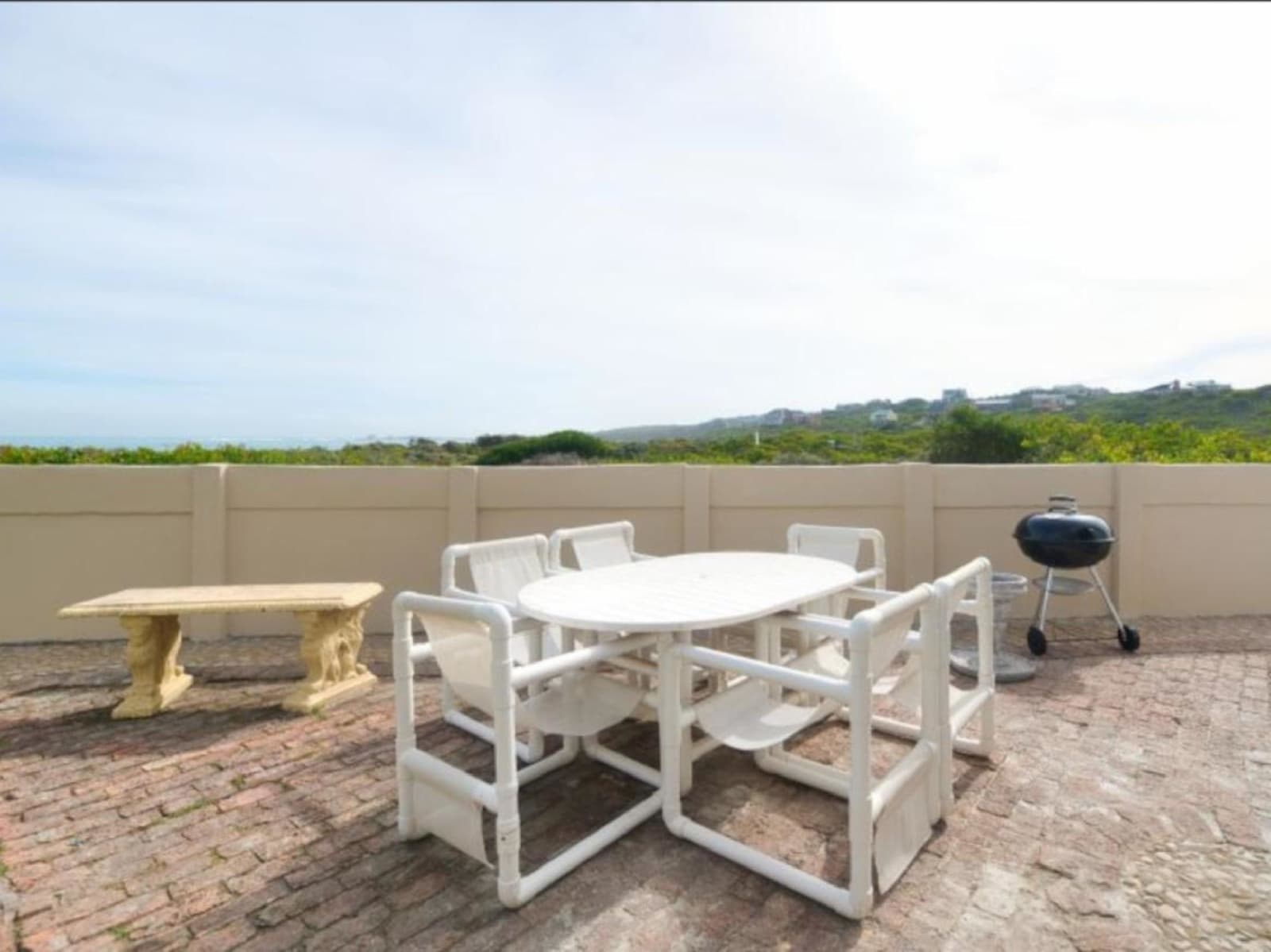 The brick-paved patio at Gans-te-Ver — outdoor dining table, a stone bench and the Weber braai, with fynbos hills beyond the wall.