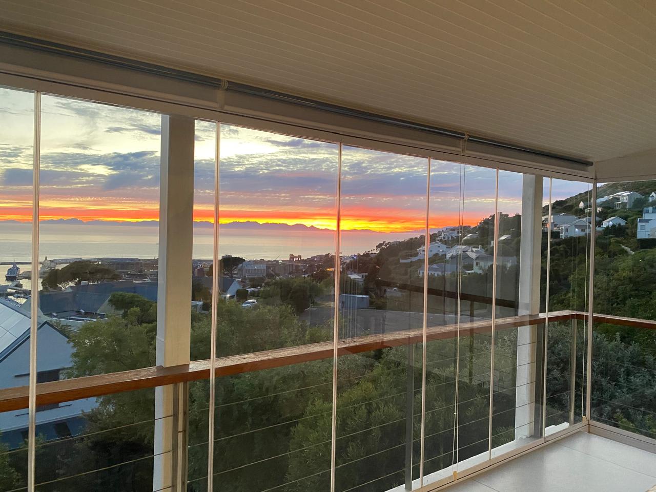Sunset from the top-floor sunroom at Gans-te-Ver — the sky burning orange over the mountains and bay, seen through the frameless sliding glass that now encloses the sea-facing balcony.