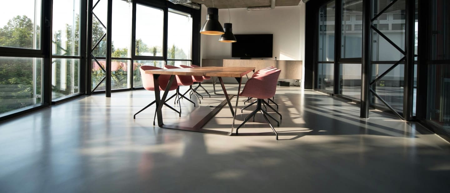 An empty meeting room with a long table and chairs, lit from a wall of windows