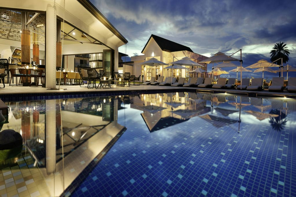 A lit resort building reflected in a still swimming pool at dusk