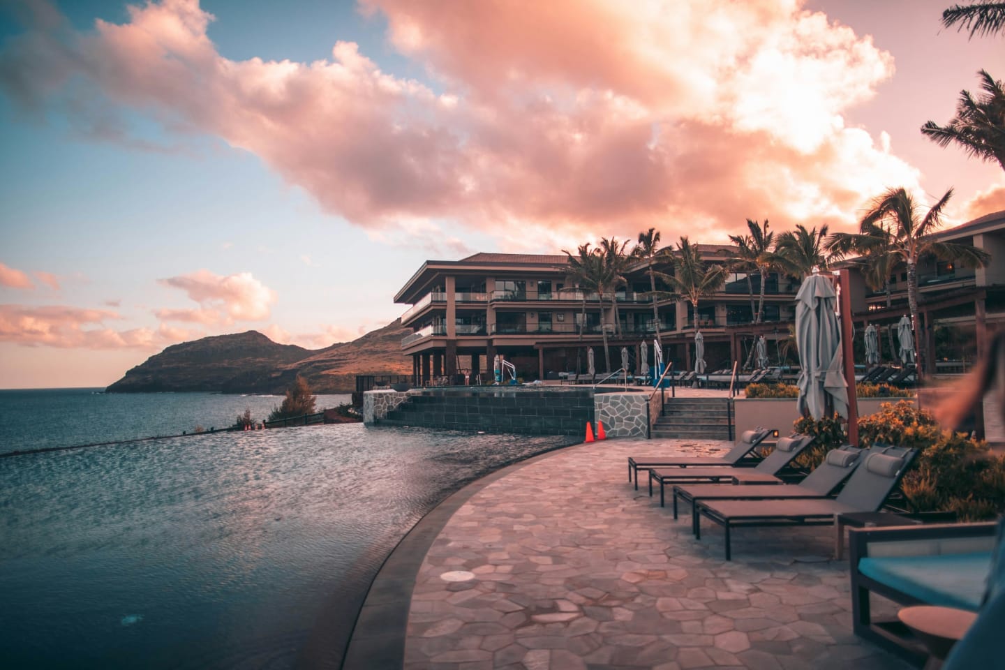 A hotel terrace above the sea at dusk, sun loungers set out along the path