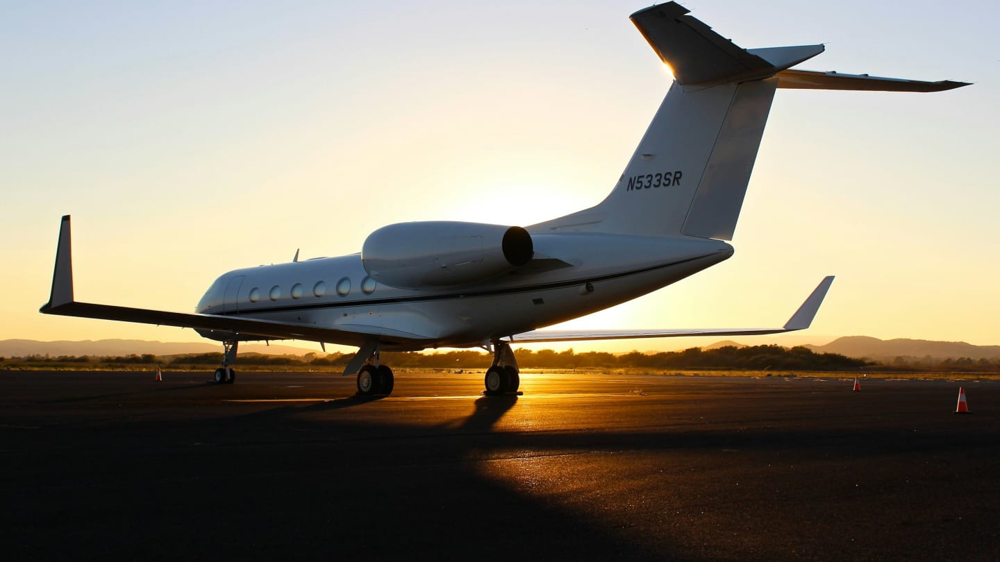 A private jet standing on a runway with the sun setting behind it
