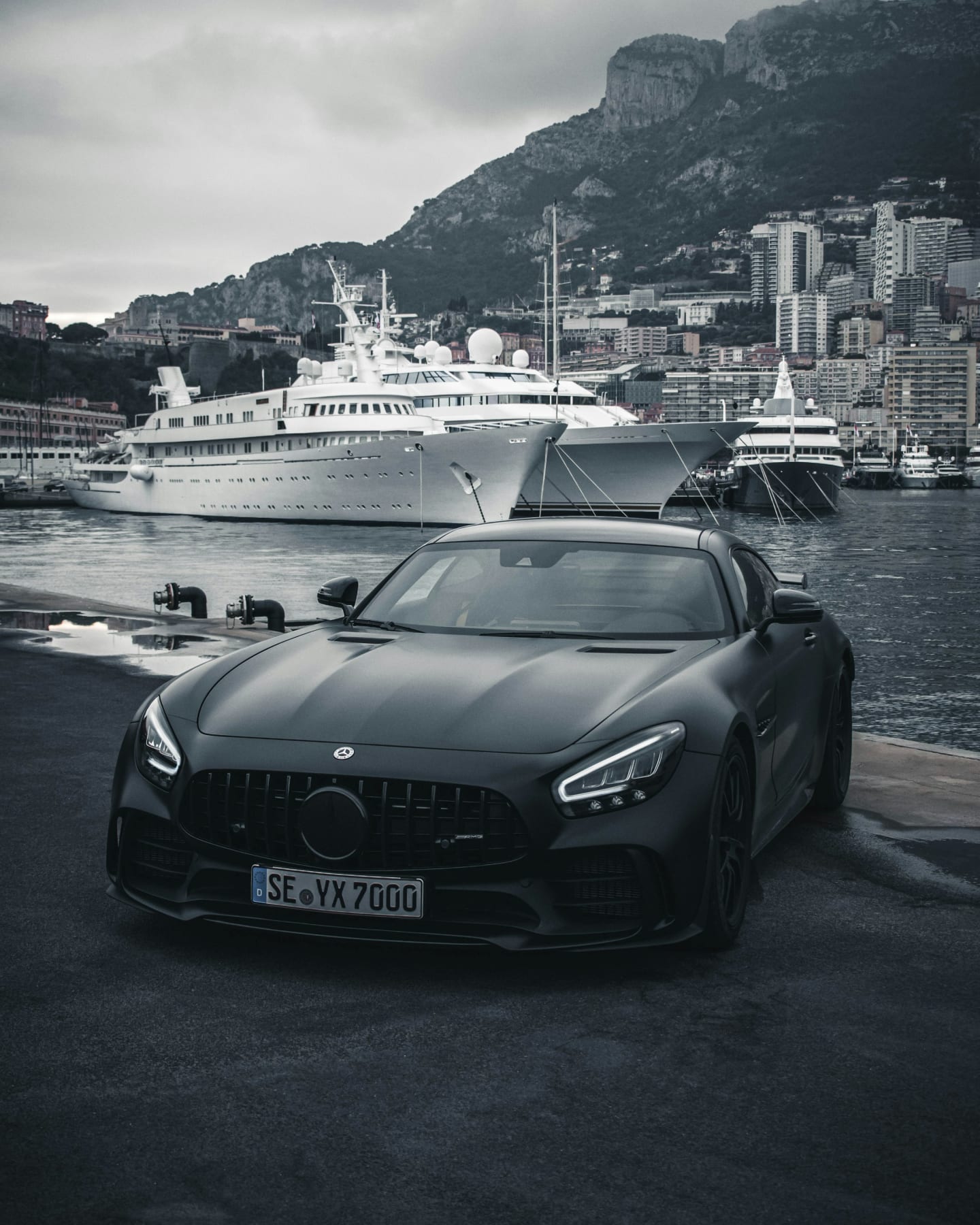 A black sports car parked on the quayside at Monaco with moored yachts behind it