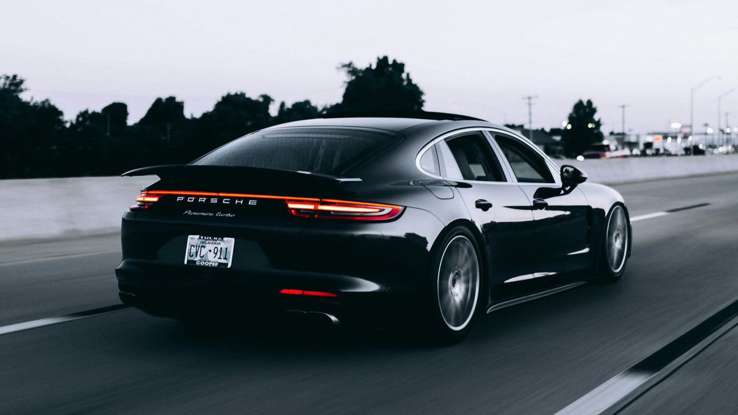A black saloon travelling a tree-lined road, photographed from behind at speed