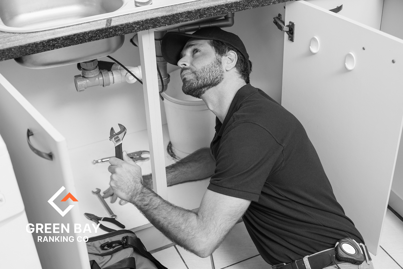Plumber repairing pipes under a kitchen sink for a Green Bay, WI local plumbing services business.