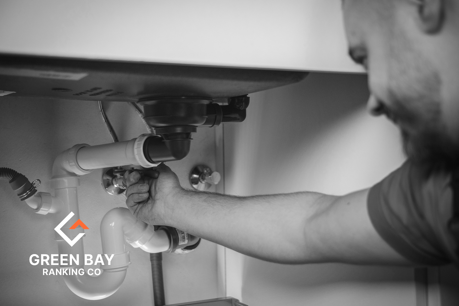 Plumber repairing drain pipes beneath a sink for a Green Bay, WI plumbing services business.