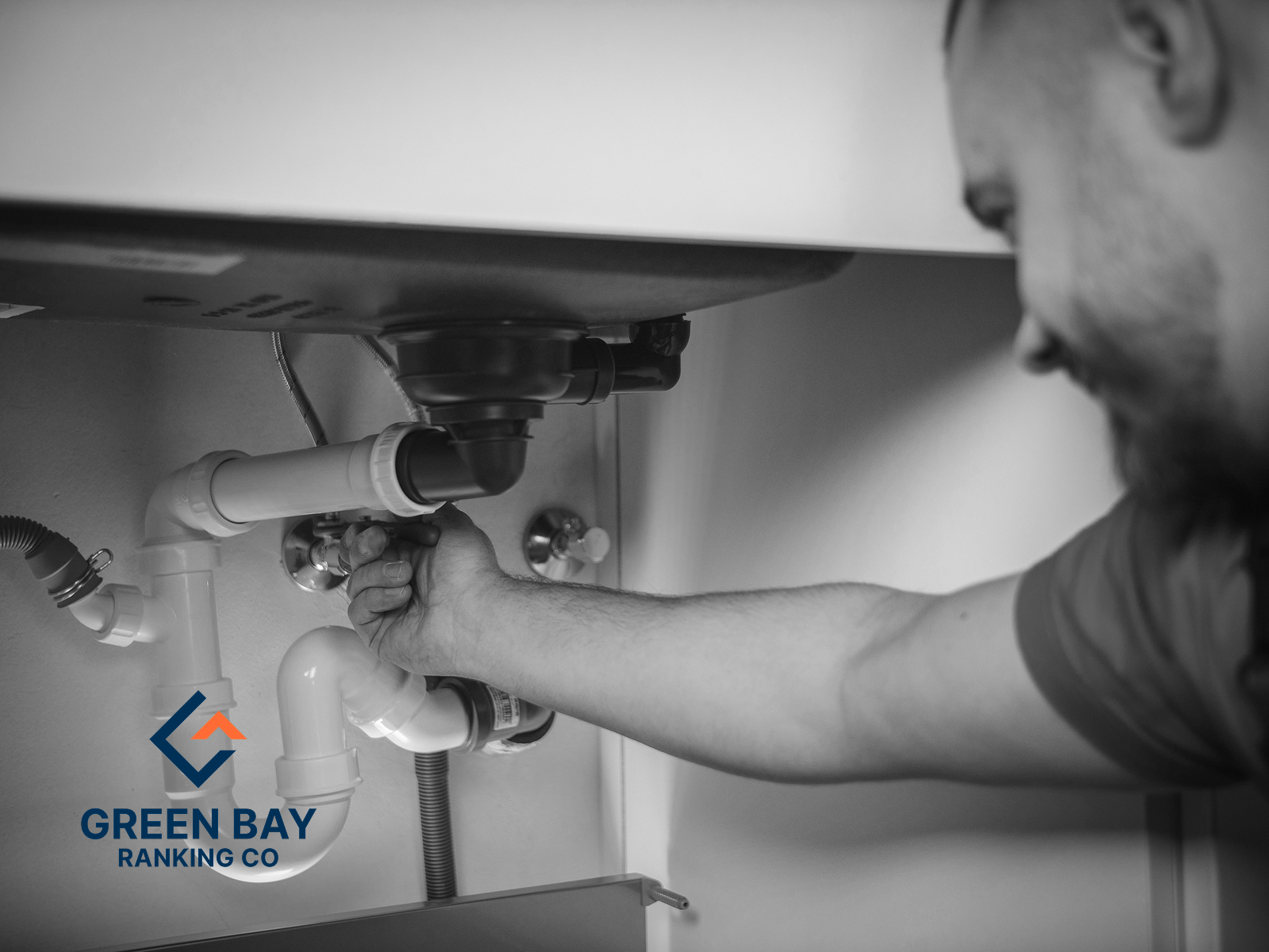 Plumber repairing drain pipes beneath a sink for a Green Bay, WI plumbing services business.