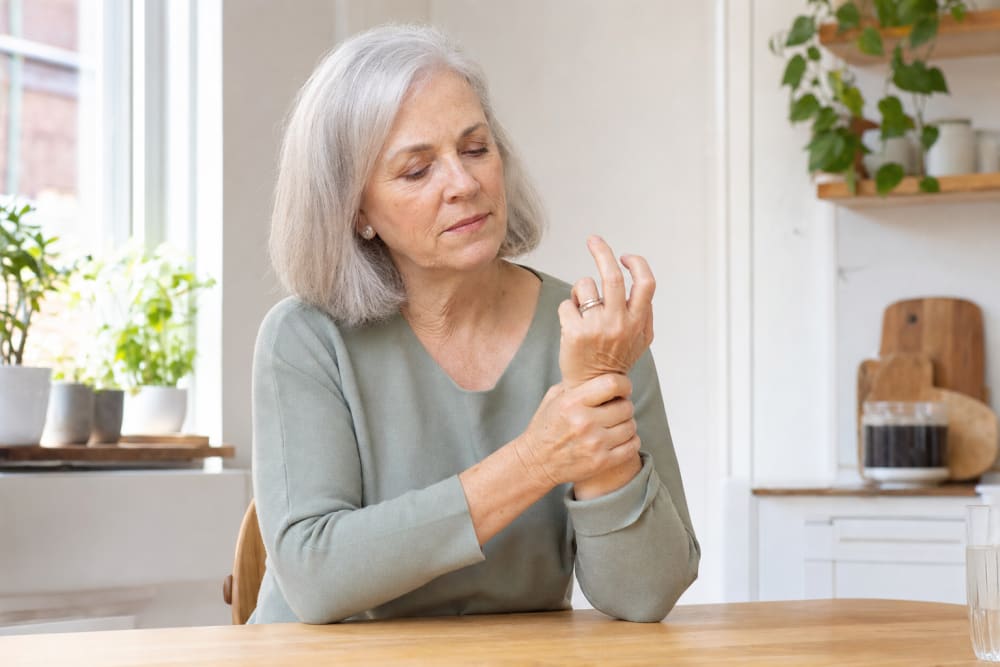 Femme senior massant son poignet douloureux, assise à sa table de cuisine