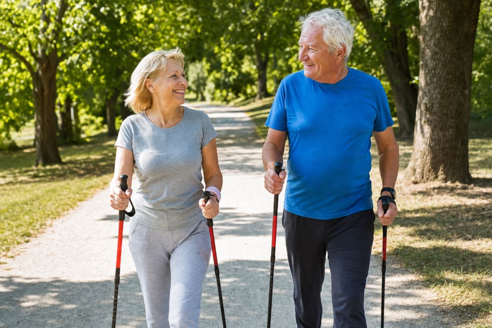 Couple de seniors souriants pratiquant la marche nordique sur un chemin de parc ensoleillé