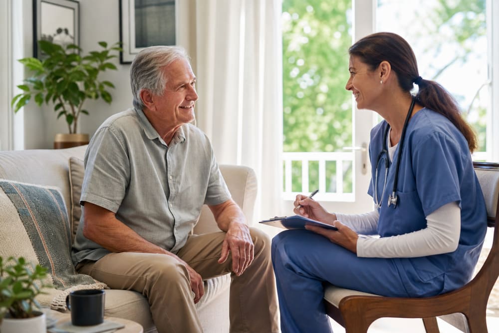 Un professionnel de santé prenant des notes lors d'une consultation à domicile avec un patient âgé dans un salon lumineux