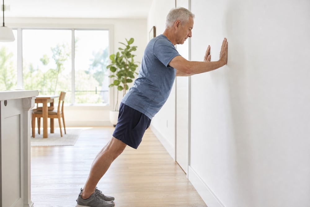 Homme de 65 ans faisant des pompes murales à domicile, mains à plat contre le mur