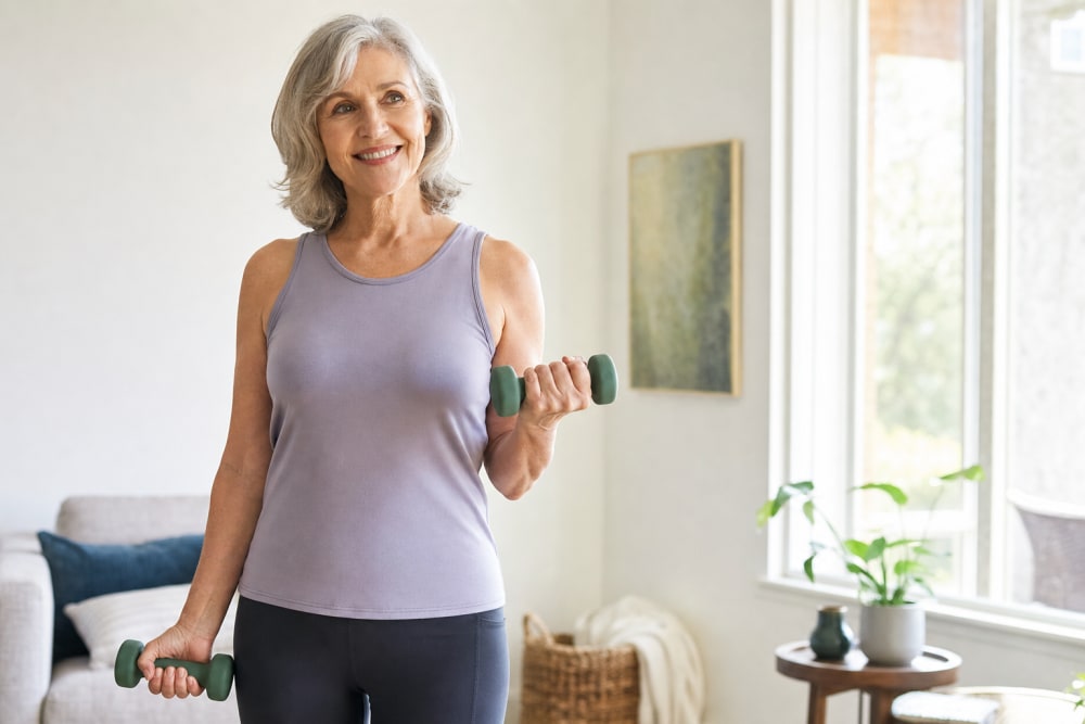 Femme de 60 ans faisant des curl biceps avec des haltères légers dans son salon lumineux