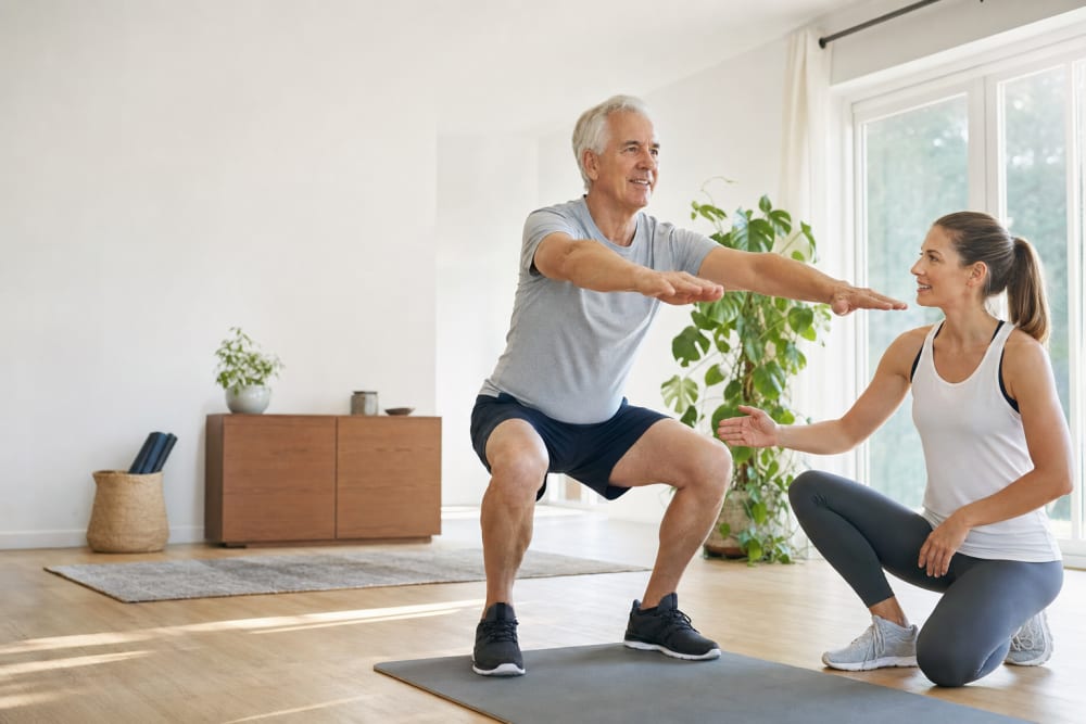 Senior réalisant un exercice de renforcement musculaire à domicile accompagné de son enseignant APA