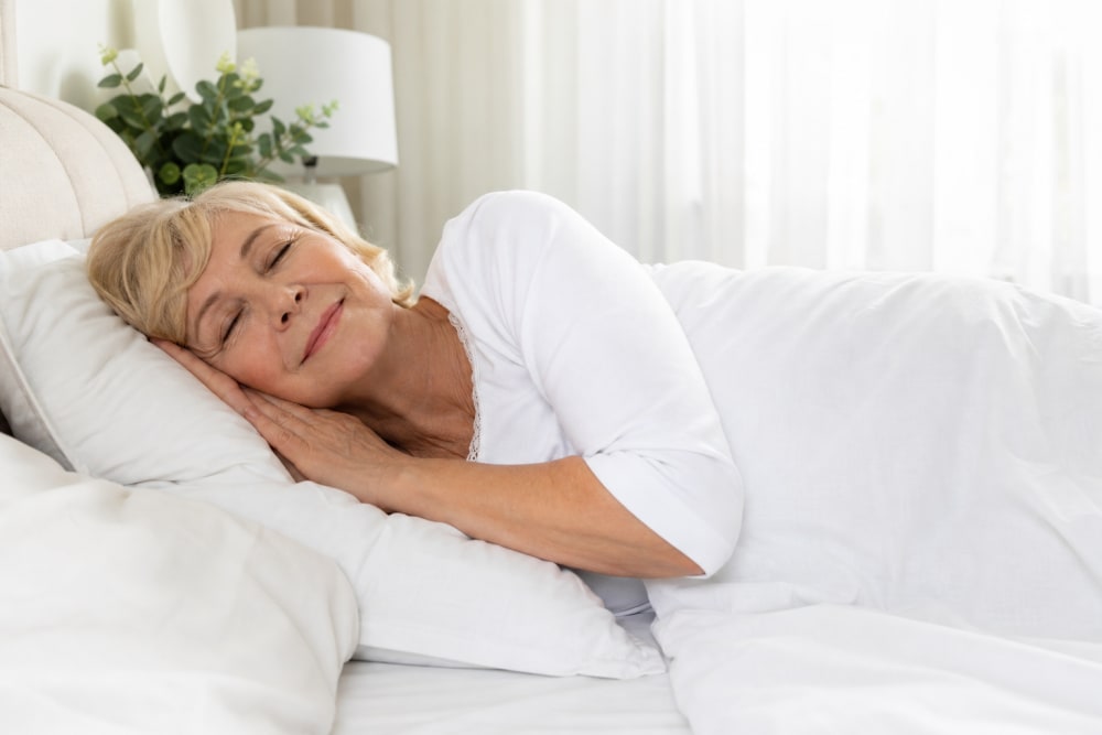 Femme senior dormant paisiblement dans une chambre lumineuse aux draps blancs