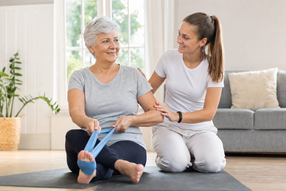 Enseignante APA guidant une femme de 67 ans lors d'une séance d'activité physique adaptée à domicile dans un salon lumineux