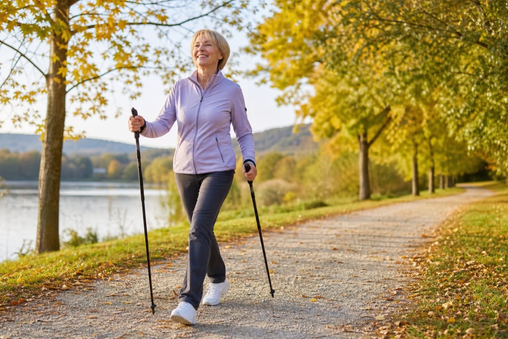 Femme pratiquant la marche nordique dans un parc ensoleillé aux couleurs d'automne, une activité douce et bénéfique pour le dos