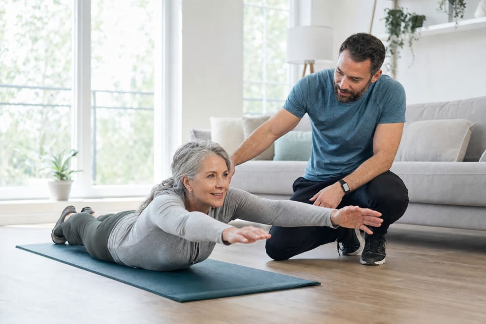 Femme en séance d'exercices de dos à domicile sur un tapis de yoga, accompagnée d'un enseignant en activité physique adaptée