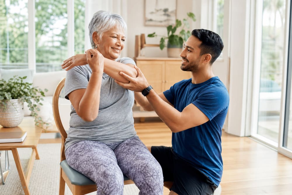 Une femme d'une soixantaine d'années réalise des exercices d'étirement à domicile avec l'aide d'un coach en activité physique adaptée