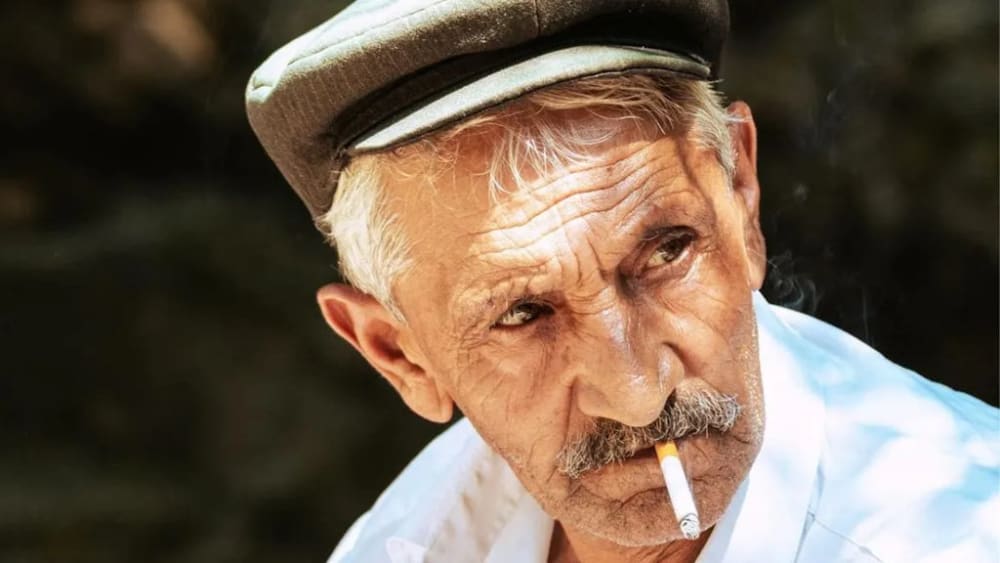 Un homme âgé fume une cigarette