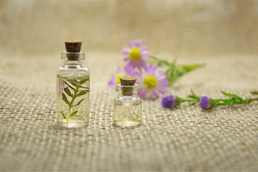 Des flacons d'huile essentielles et des fleurs violettes sont posés sur un tissu