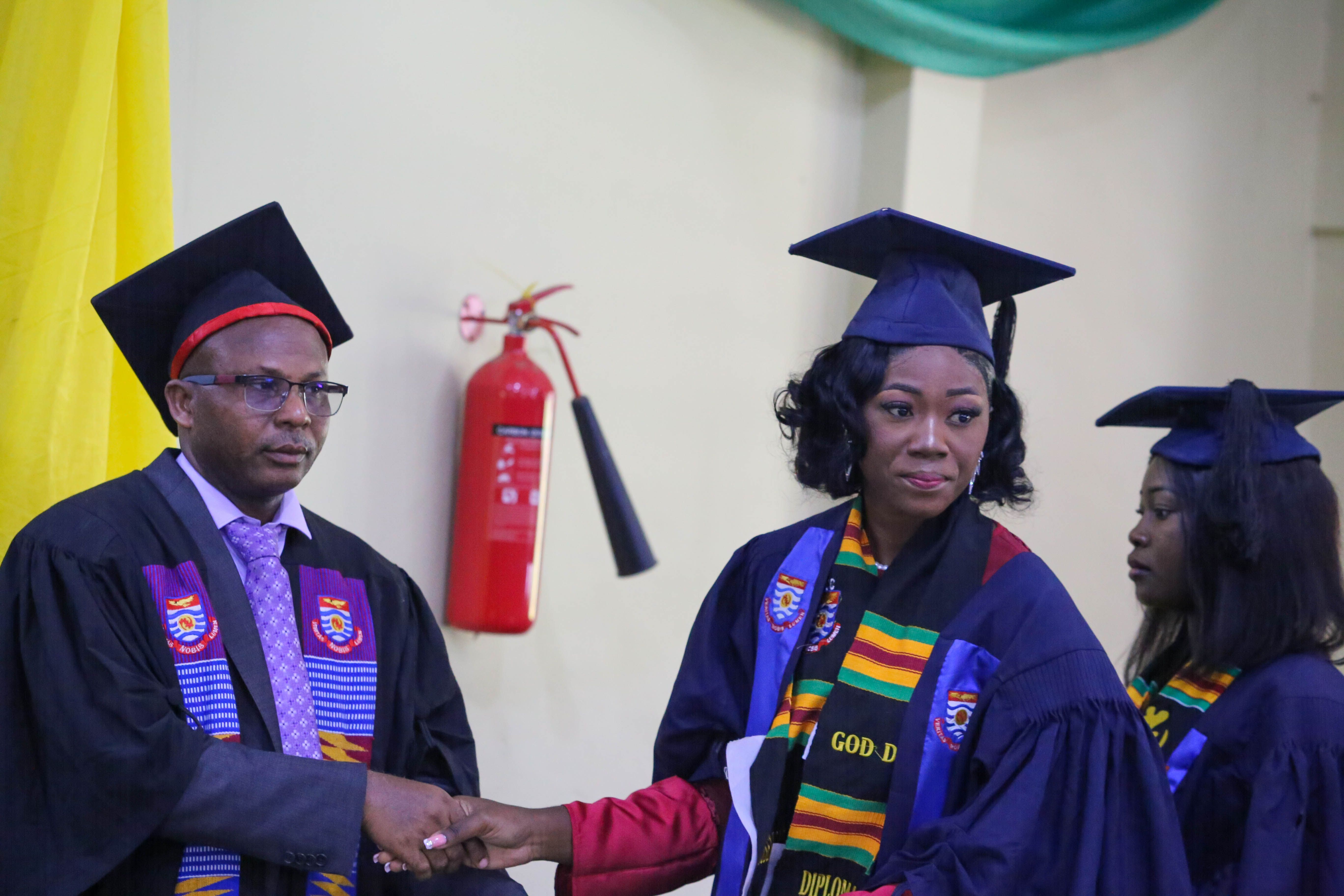 Graduate in cap and gown shaking hands with a faculty member at a ceremony.