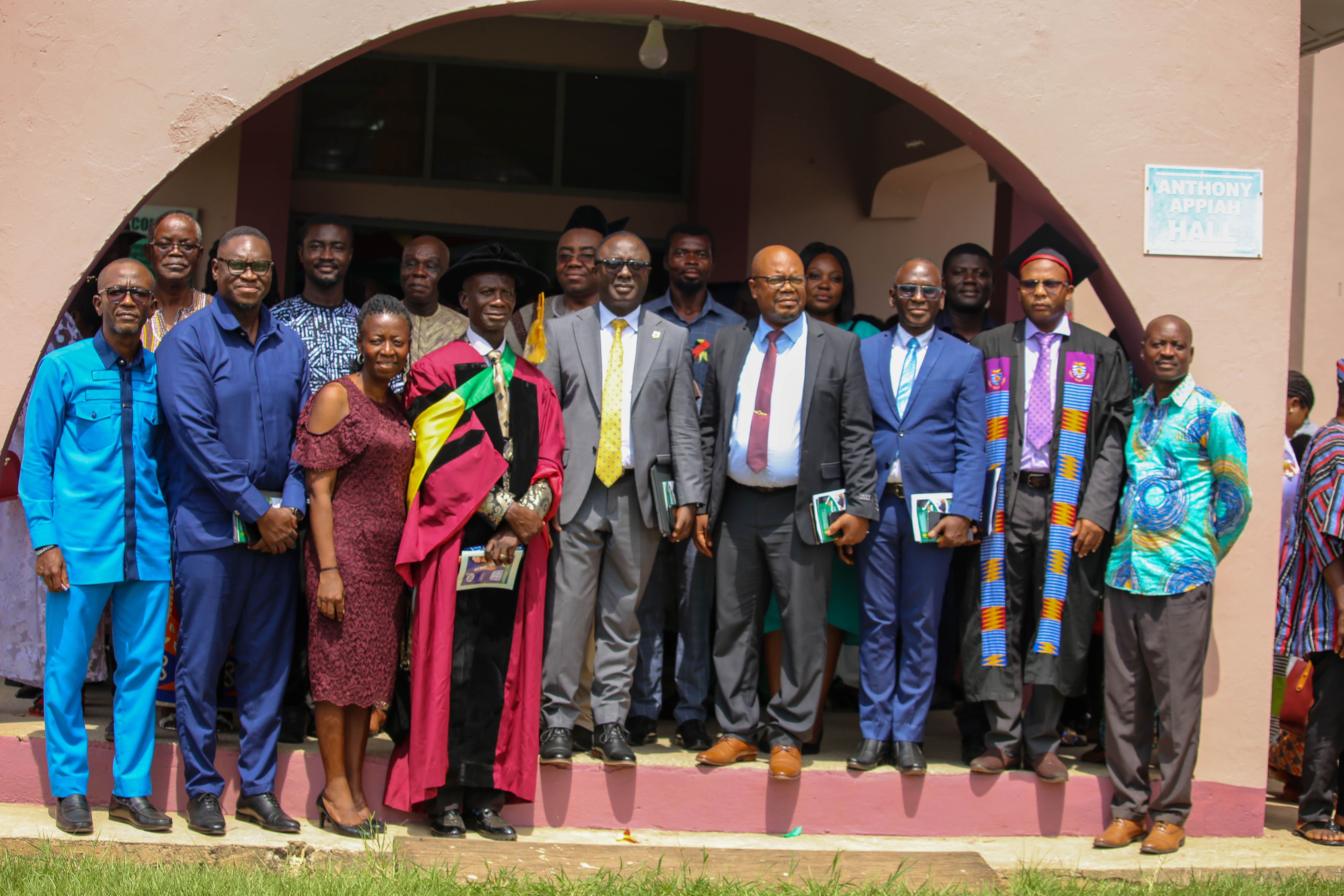 Diverse group of professionals in formal and traditional attire posing outside a building.