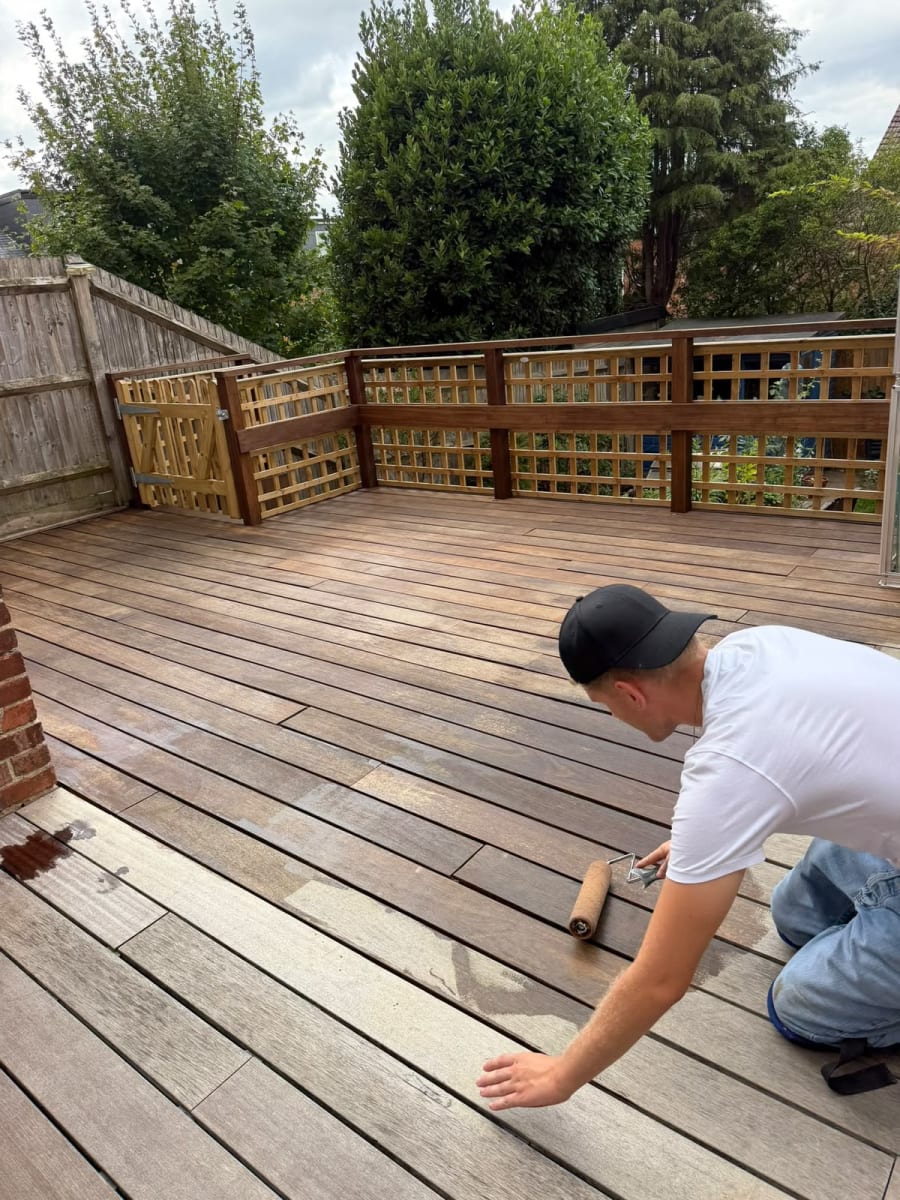 Gardener applying decking oil with a roller, showing restored and untreated boards side by side