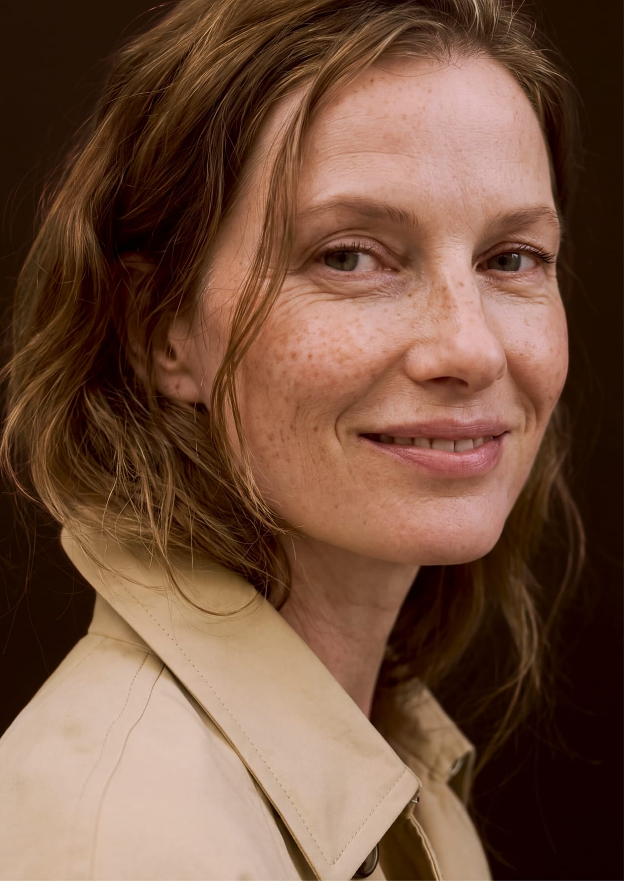 Woman with freckles in a trench coat, smiling