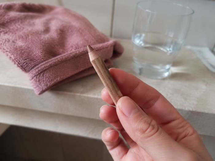 Contour Pencil held between two fingers over a bathroom shelf