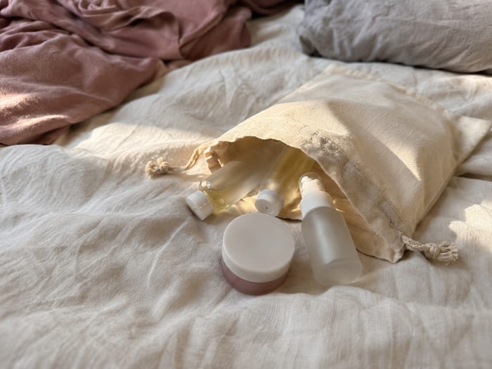 An open cotton bag on a bedspread, a few small bottles beside it