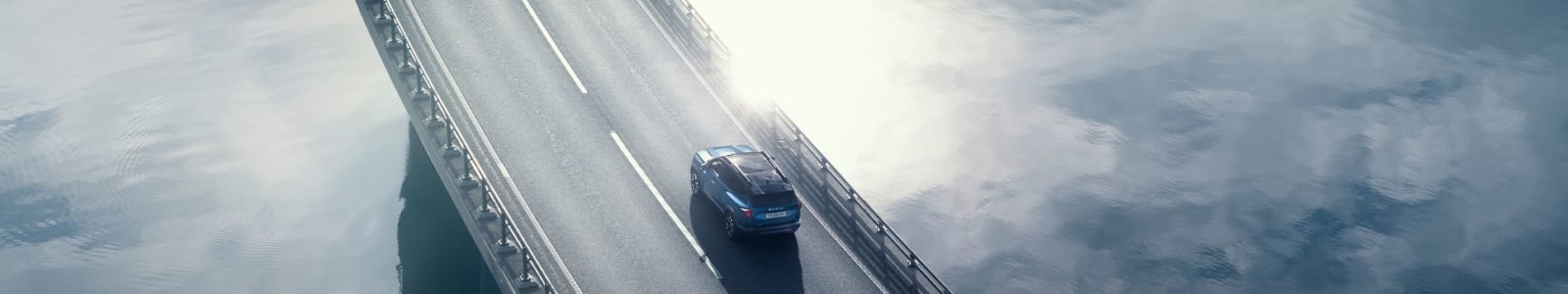 Sininen Dacia Bigster ajamassa pitkällä sillalla, alapuolella vettä.