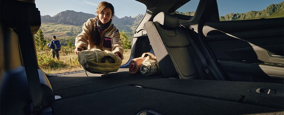 Nainen pakkaamassa laukkua Hyundai Tucsonin takakonttiin.