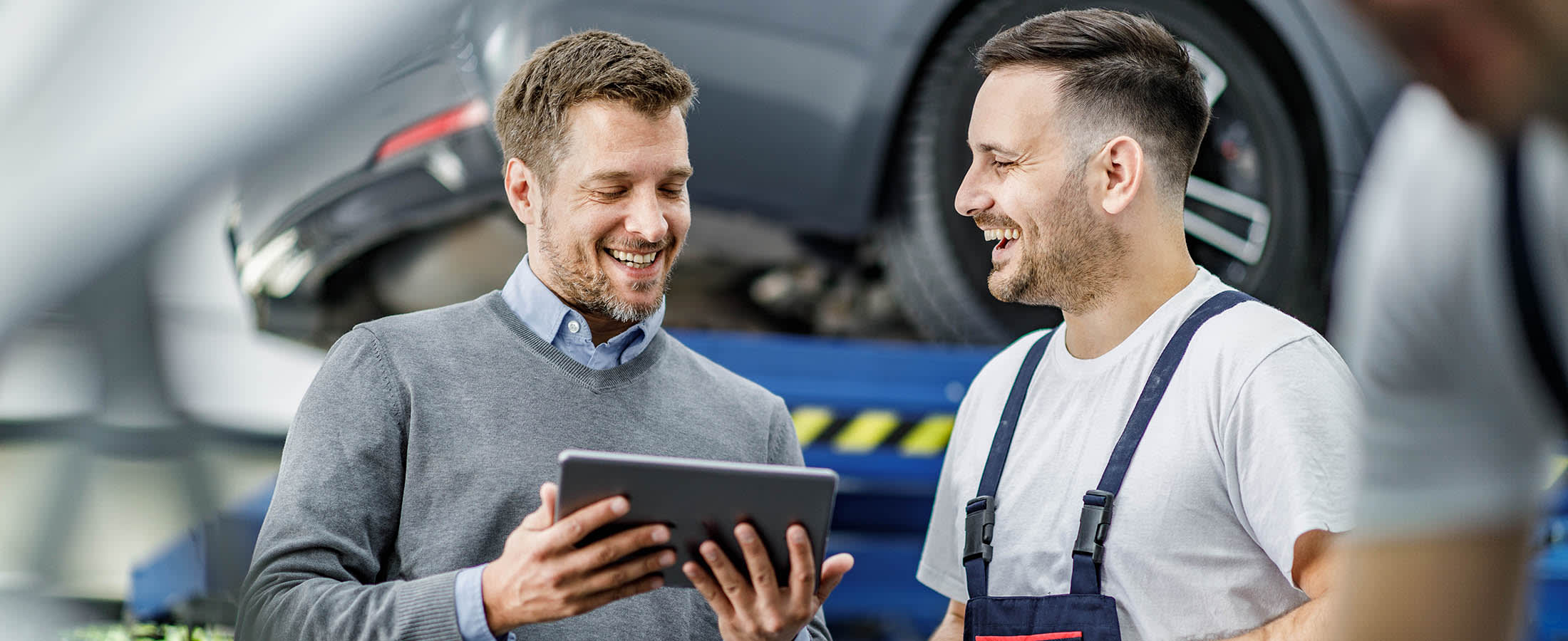 Kaksi miestä autohuollossa. Vasemmanpuoleisella miehellä on tabletti kädessä.