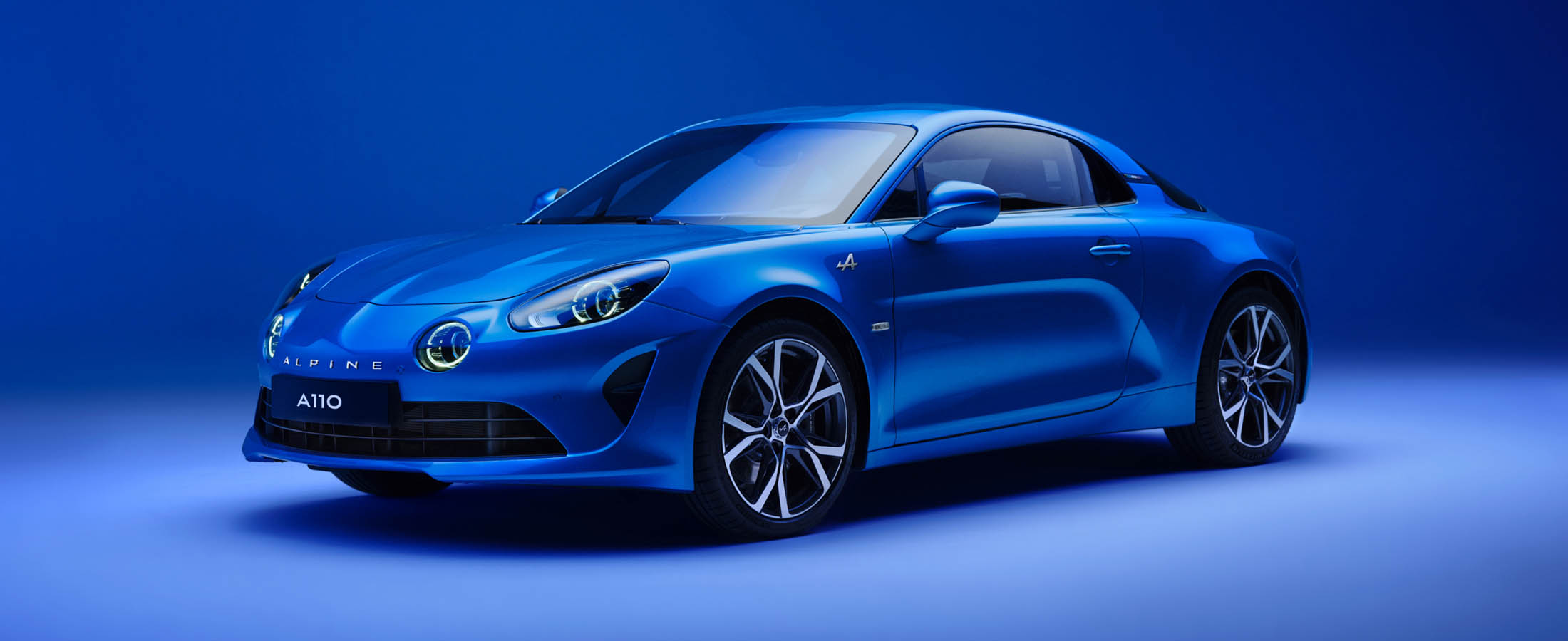 Sininen Alpine A110 -urheiluauto sinisellä taustalla