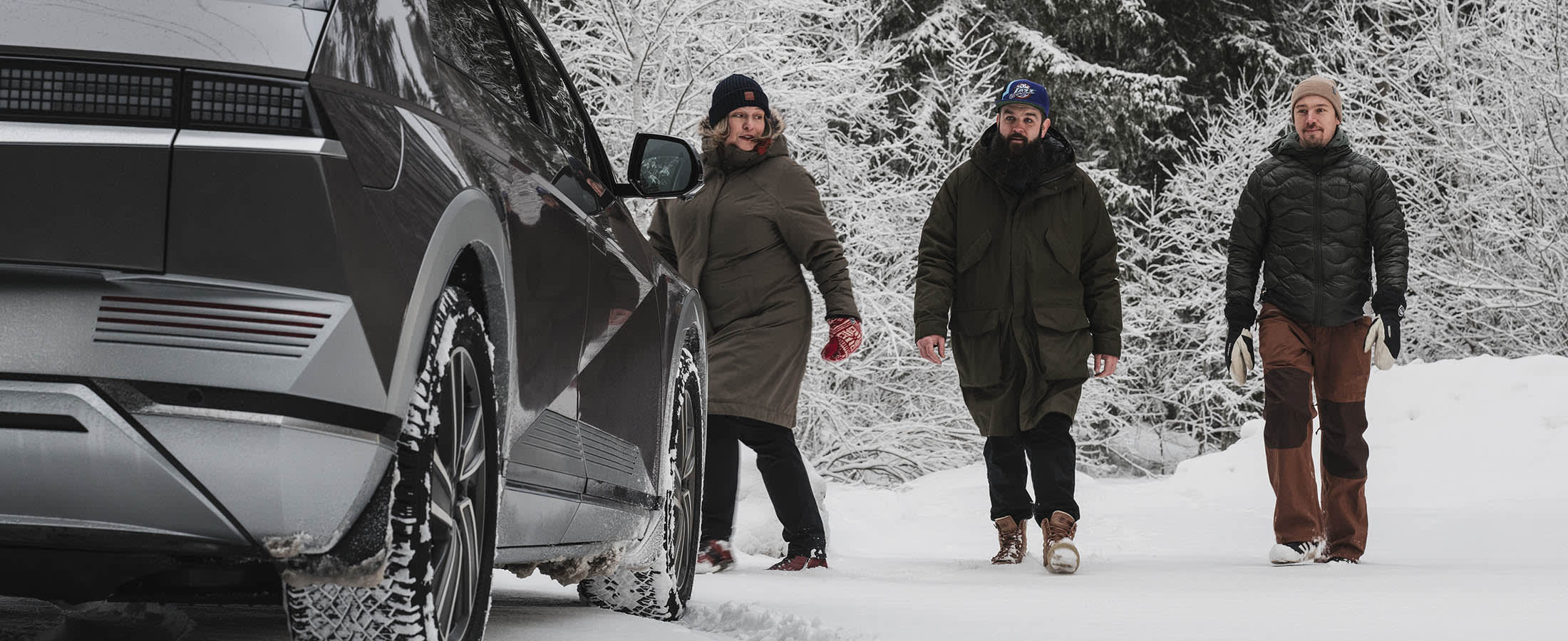 Kolme ihmistä kävelee IONIQ 5 autolle talvimaisemassa