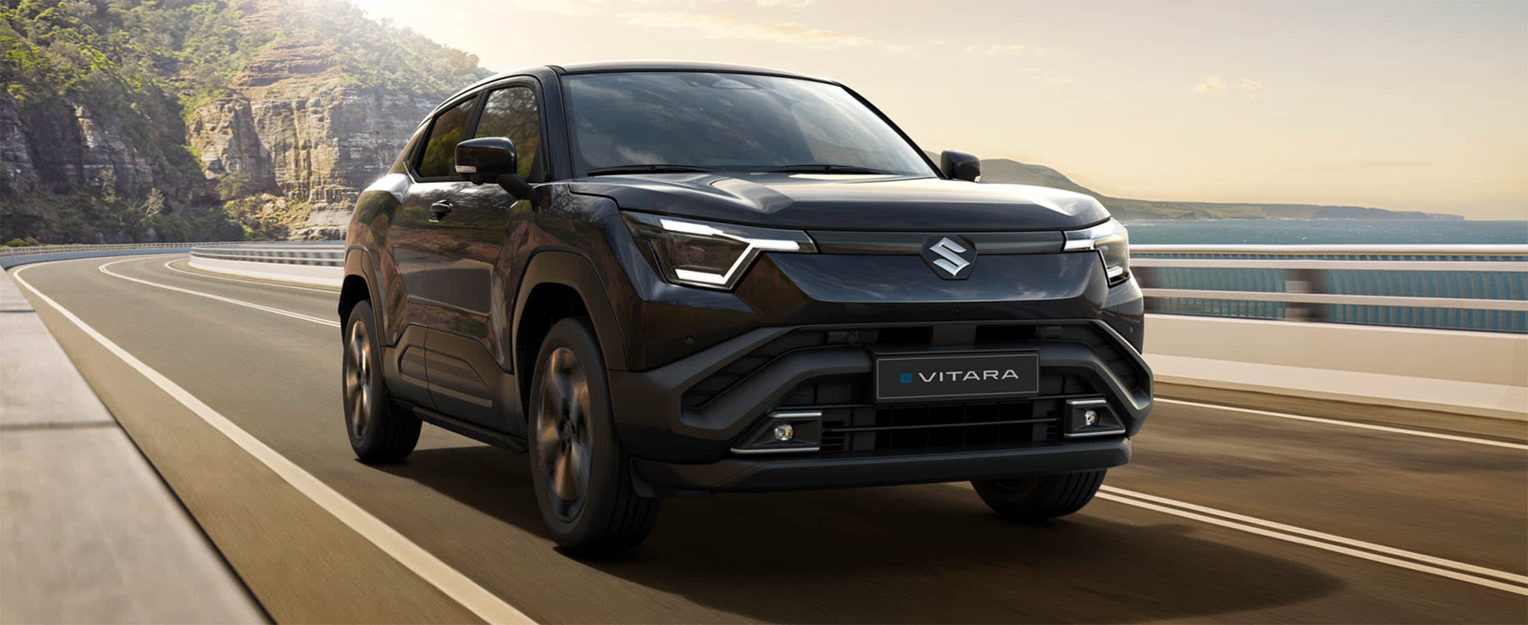 Suzuki E Vitaralla ajetaan tiellä. Taustalla on kalliomaisemaa ja meri.
