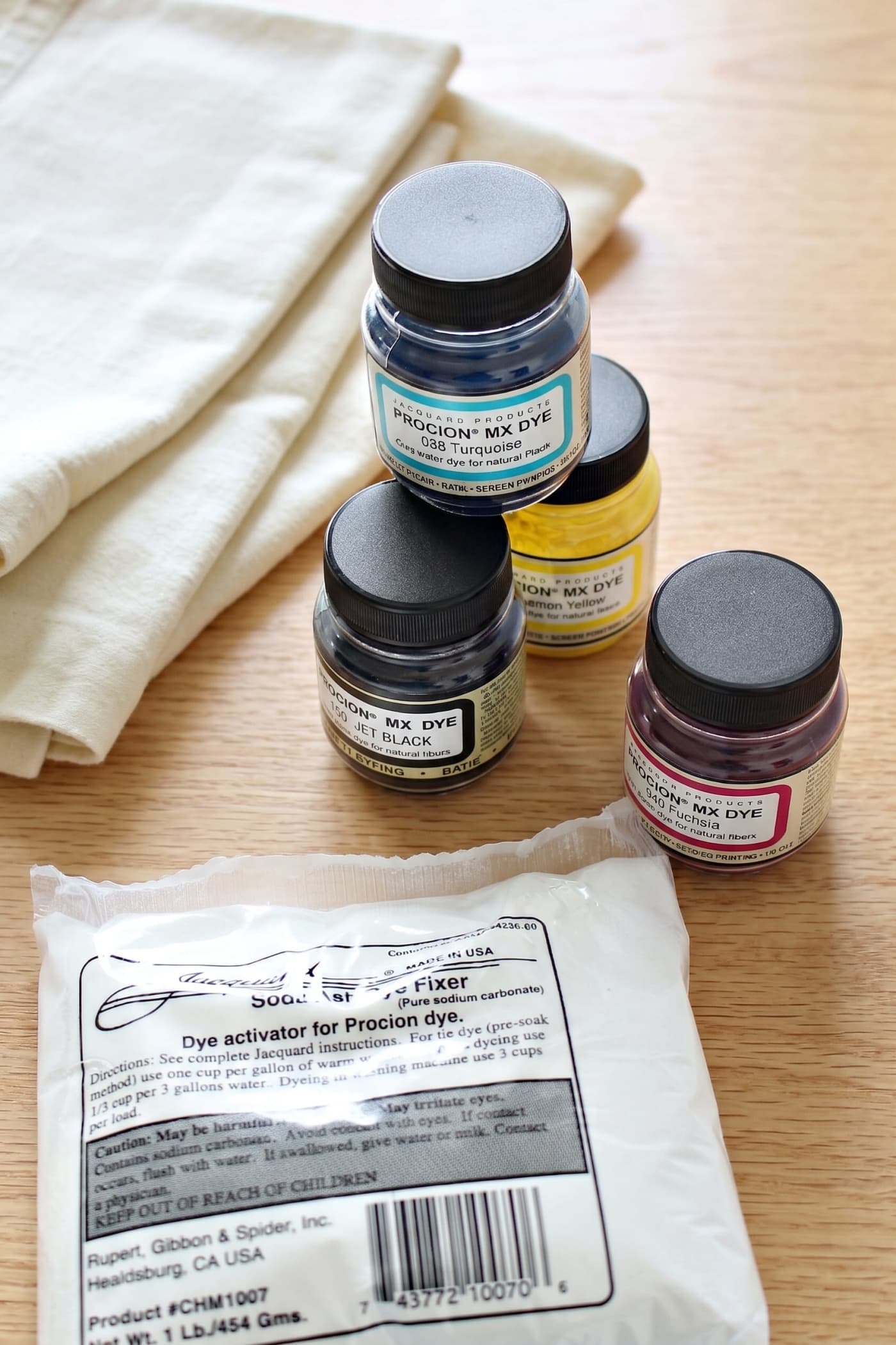 Procion dye jars and soda ash fixer beside a folded blank.