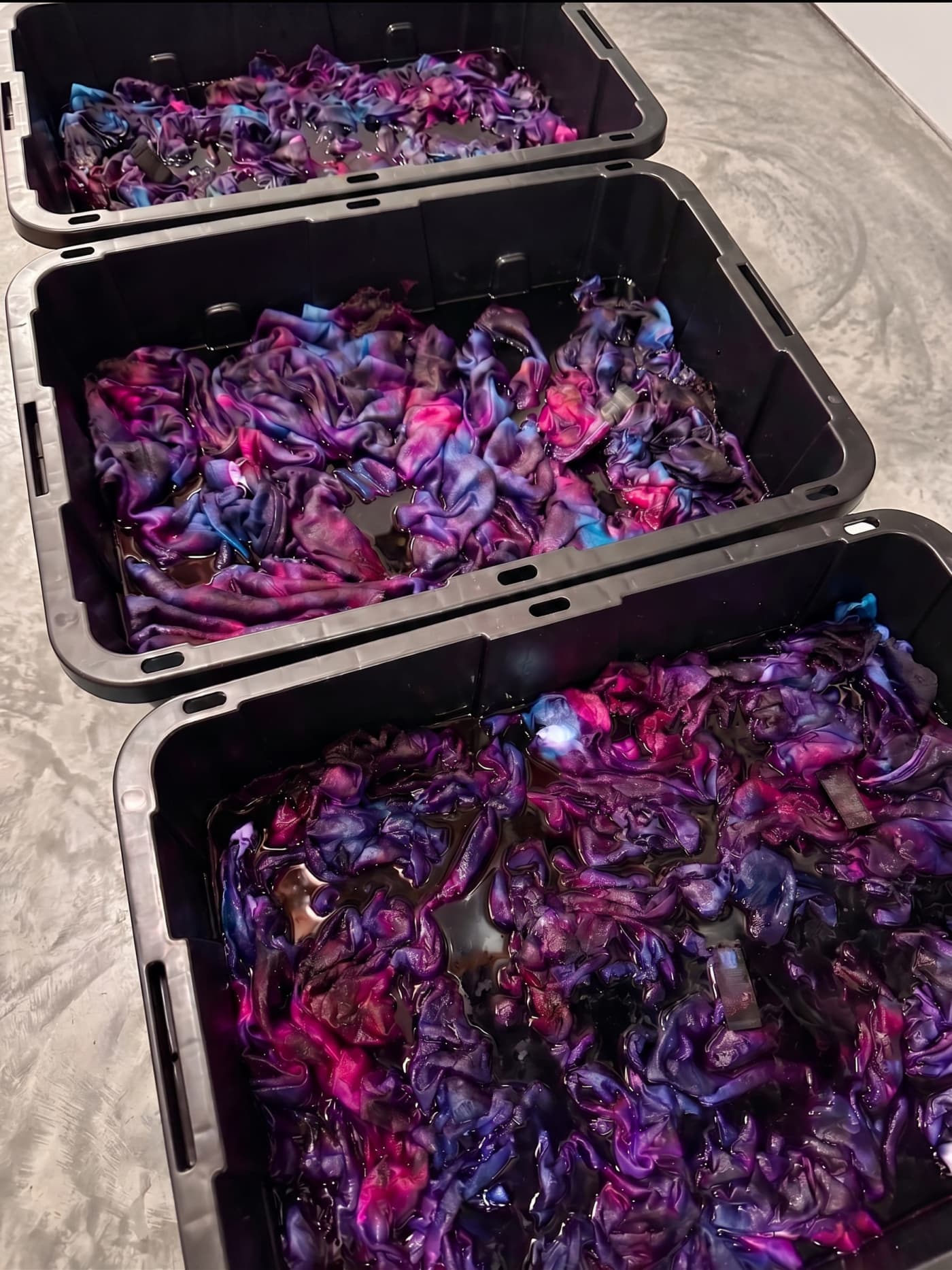 Three totes of shirts soaking in purple dye.