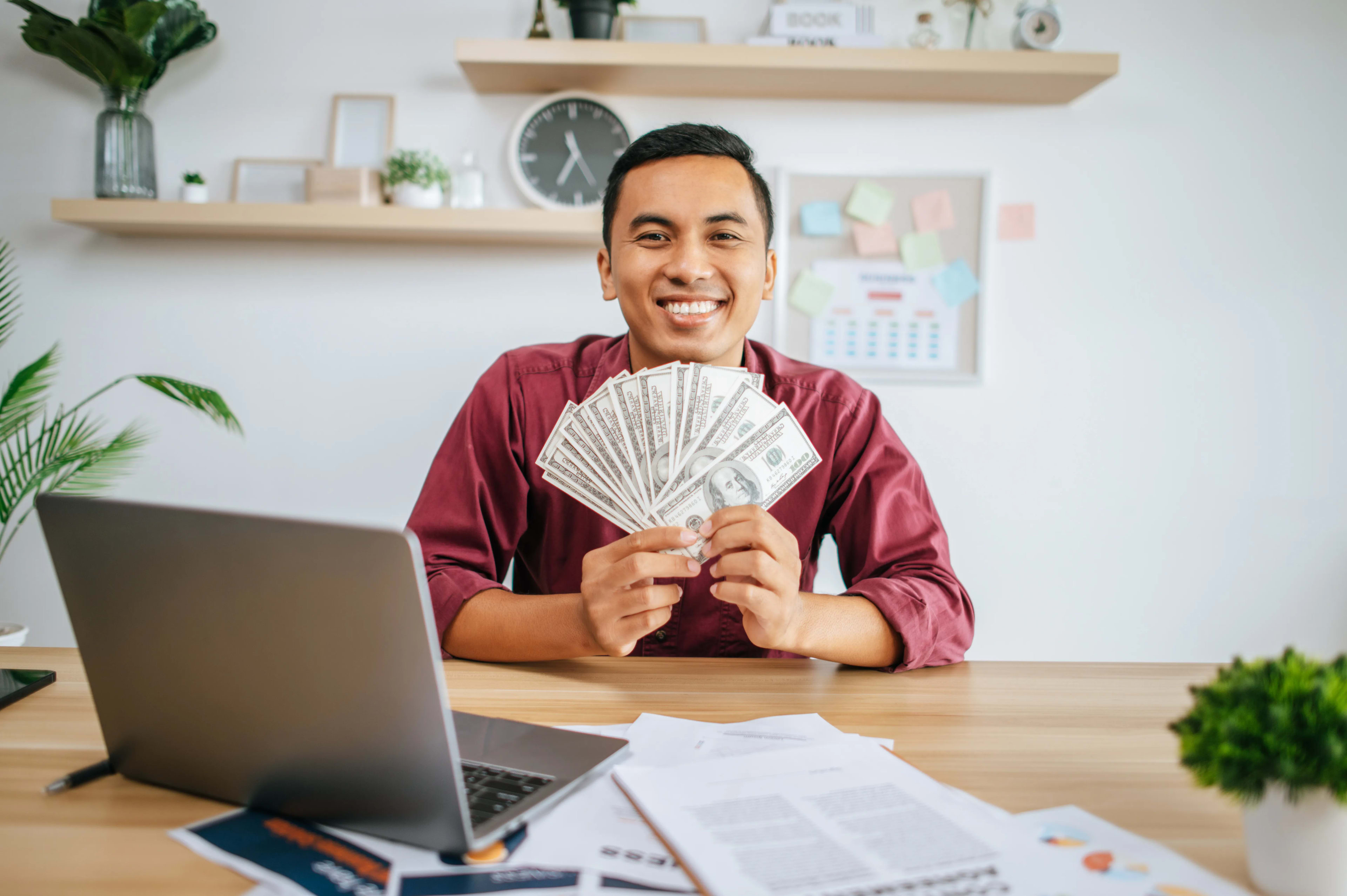 man-working-office-holding-money-with-laptop-documents-desk
