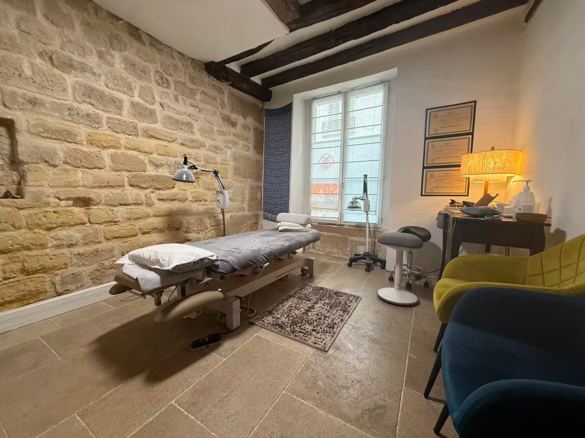 La salle de soin du cabinet, avec sa table de soin, ses murs de pierre et ses poutres anciennes.