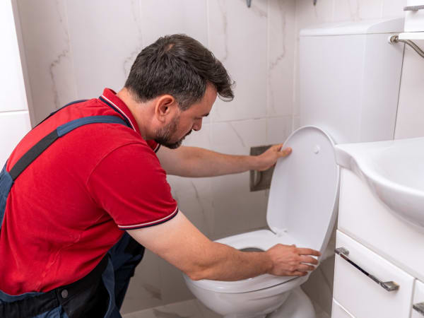 Plombier débouchant un WC dans une salle de bain moderne