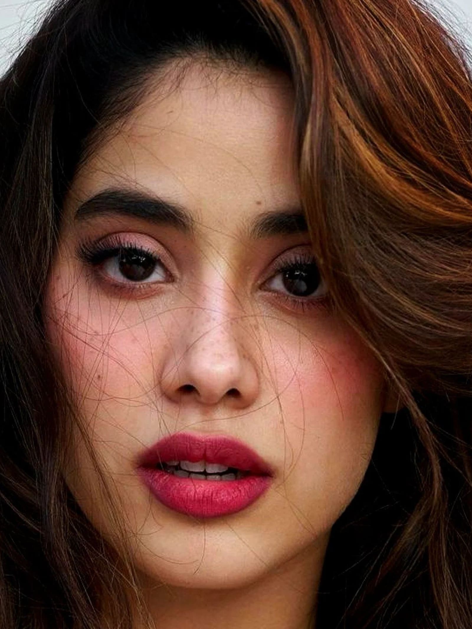 A very close-up portrait of Janhvi Kapoor, featuring her dark eyes, full lips with fuchsia lipstick, and wavy brown hair framing her face.