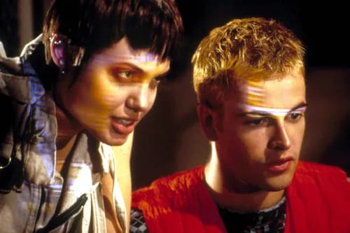 Angelina Jolie as Kate Libby, also known as Acid Burn, in a memorable scene from the 1995 film Hackers. Angelina Jolie with short dark hair and multiple ear piercings, wearing a light jacket, looking intently with horizontal light patterns across her face, from the movie Hackers.